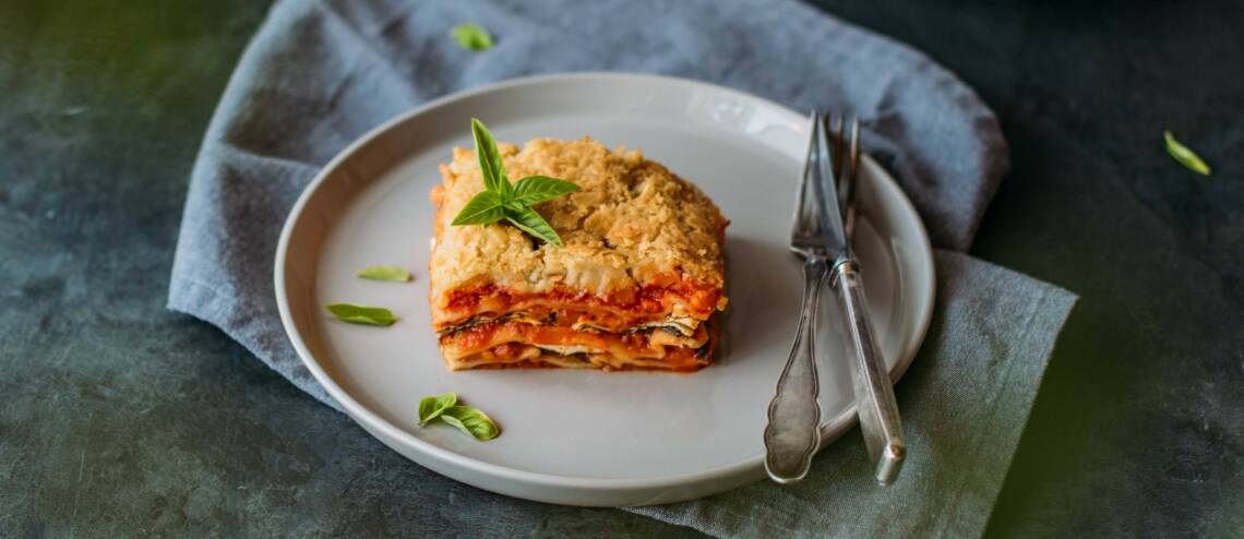 Lasagne mit Kürbis-Tomaten-Ricotta Füllung auf beigem Teller vor dunkelgrauem Hintergrund. Von schräg oben fotografiert.