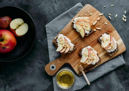 Brotscheiben mit Hüttenkäse, Apfelscheiben und Mandelsplitter auf einem Holzbrett.