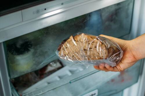 Brot in Plastikhülle und Hand vor Gefrierfach.