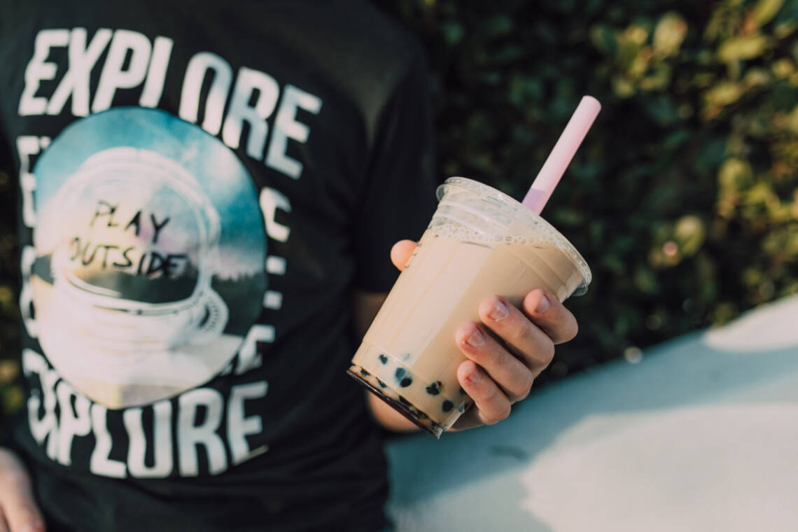 Bubble Tea in einem Plastikbecher, von jemanden in einem schwarzen T-Shirt gehalten.