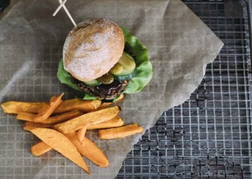 Veganer Burger mit selbstgemachten Süßkartoffelpommes auf einem Gitter mit Backpapier. Von oben fotografiert.
