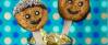 Smiley-Kekse auf Holzstäbchen in eine Dose gesteckt vor blauer Pünktchentapete