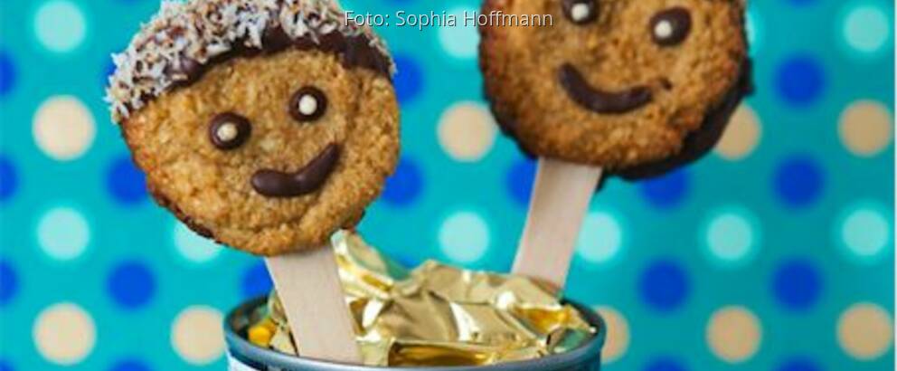 Smiley-Kekse auf Holzstäbchen in eine Dose gesteckt vor blauer Pünktchentapete