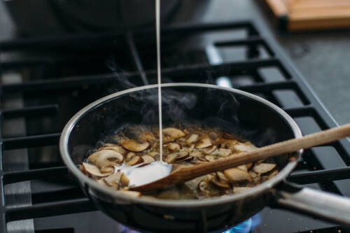 Wie du Champignons gesund aufwärmen kannst, erfährst du in diesem Artikel. Auf dem Bild ist eine mit Pilzen gefüllte Pfanne zu sehen, von der Seite fotografiert.