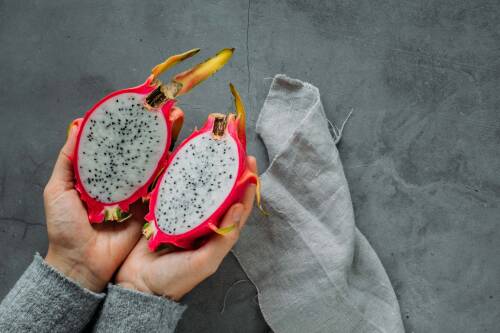 Drachenfrucht aufgeschnitten in zwei Händen vor hellem Hintergrund.