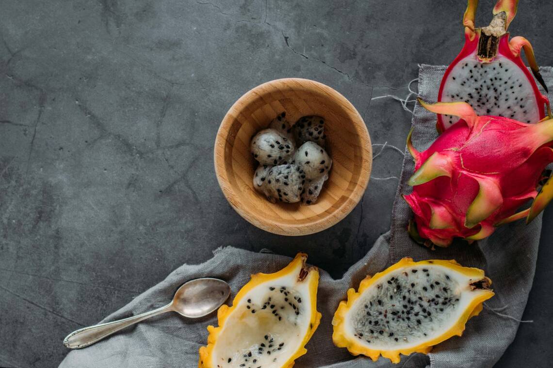 Drachenfrucht aufgeschnitten in Holzschüssel vor grauem Hintergrund.