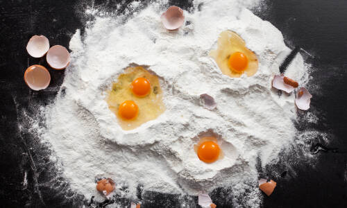 Aufgeschlagene Eier in Mehl großflächig auf schwarzem Tisch verteilt