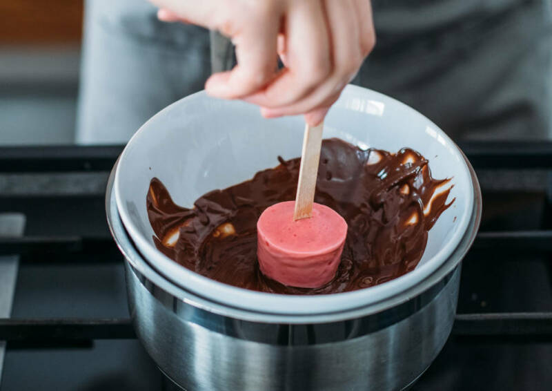 Ein selbstgemachtes Erdbeereis wird in geschmolzene Schokolade getaucht.
