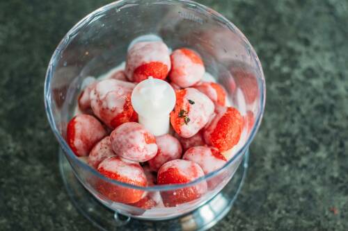 Erdbeeren in Mixer mit veganer Milch vor dunklem Hintergrund.