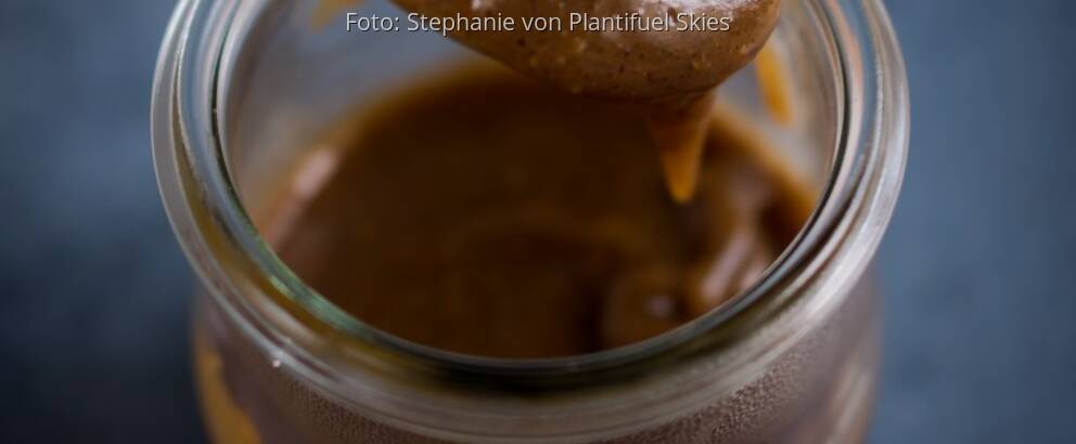 Glas mit selbstgemachter Erdnuss-Karamell-Sauce auf dunkler Platte