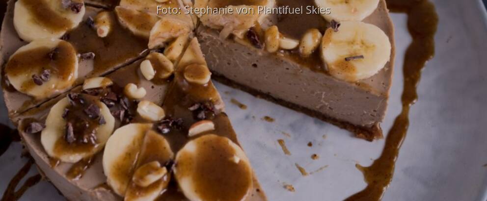 Torte aus Erdnussbutter auf großer heller Platte, dekoriert mit Bananenscheiben, Pinienkernen und Karamell