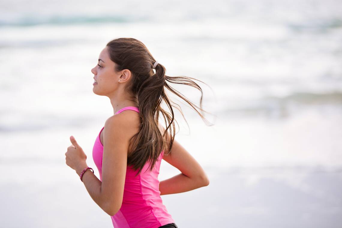 Eine Frau mit pinkem Oberteil joggt, im Hintergrund das Meer