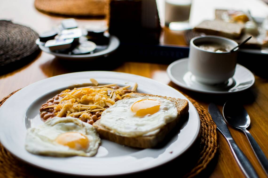 Ein Frühstücksteller mit Bohnen und Ei-Toast, im Hintergrund eine Tasse Kaffee