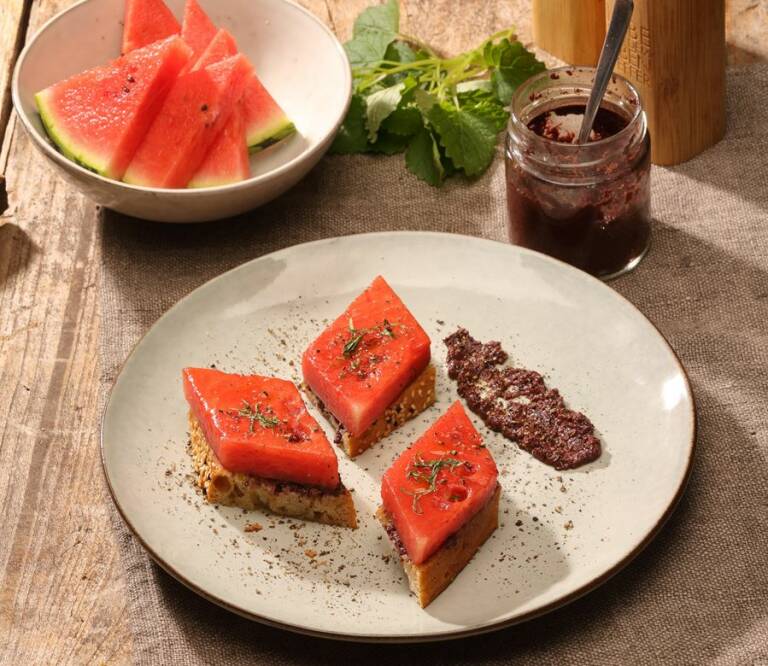 Teller mit gebratener Wassermelone, Olivnepaste auf Holztisch