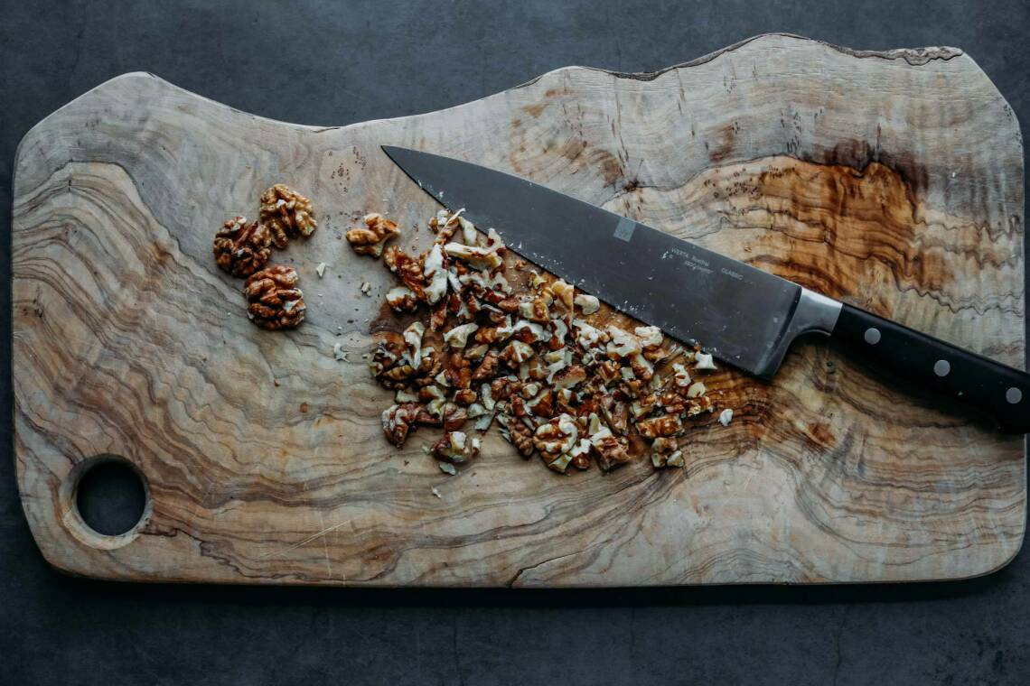 Gehackte Walnüsse mit einem Messer auf einem Holzbrett.