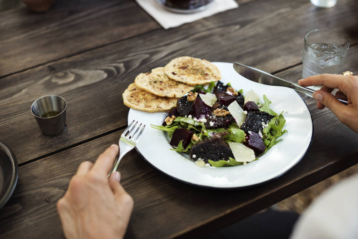 weißer Teller mit Salat (Blattsalat, rote Bete, Käse) auf einem Holztisch