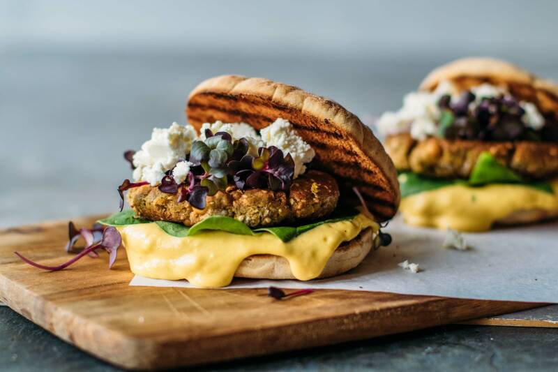 Leckeres vegetarisches Burger Patty im Bun  mit leckerer Soße und Feta vor hellgrauem Hintergrund, von der Seite fotografiert.
