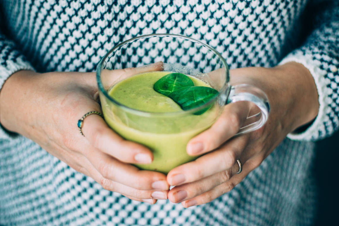 Frau schenkt grünen Smoothie aus einem Krug in ein Glas