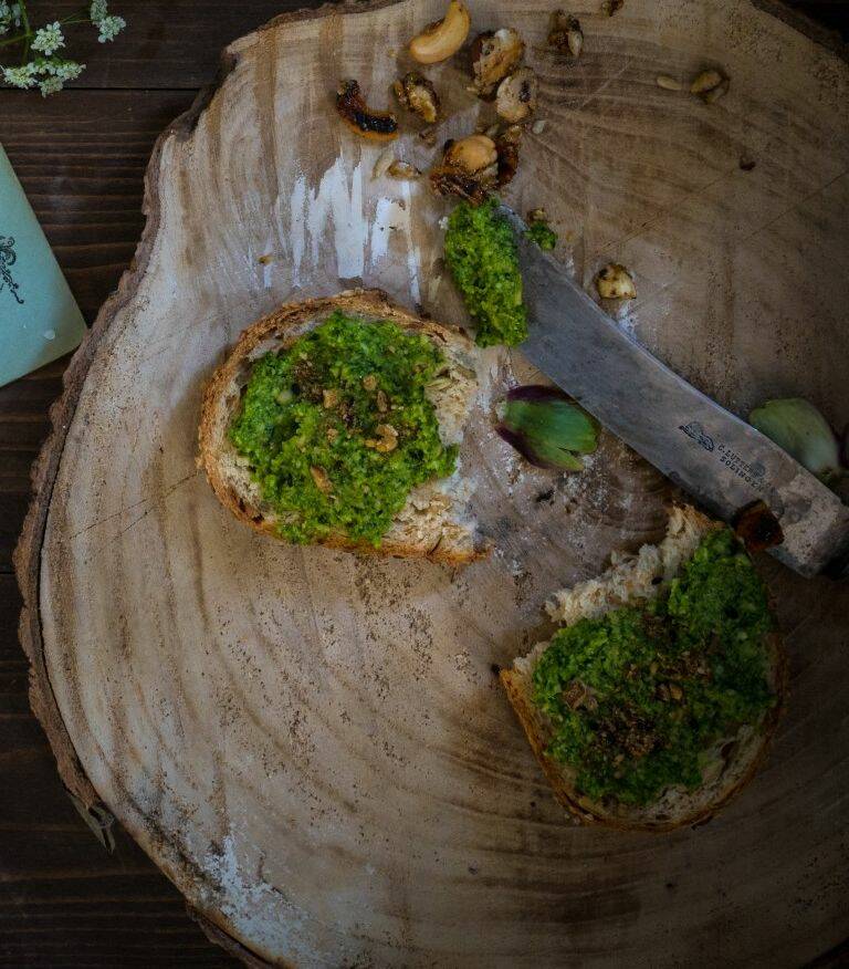 Holzscheibe mit zwei Brotscheiben mit Grünkohlpesto und Messer