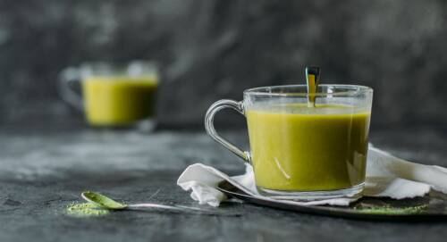 Grüner Zuckerhutsalatsmoothie in einer Tasse, darin ein Löffel. Hintergrund ist grau, von vorne fotografiert.