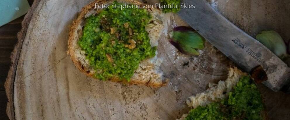 Holzscheibe mit zwei Brotscheiben mit Grünkohlpesto und Messer