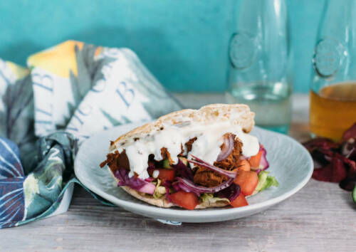 Leckeres Jackfruit Gyros im Fladenbrot, dazu knackiger Salat und Tomaten auf einem Teller. Von vorne fotografiert.