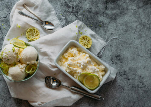 Selbst gemachtes Joghurt-Eis aus 3 Zutaten in einer großen Keramikform und einer Schüssel von oben fotografiert mit Zitronenscheiben dekoriert