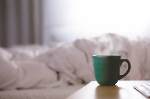 Kaffee ist ein natürlicher Stoffwechsel-Booster. Dennoch sind die Auswirkungen gering. Zu sehen ist eine dampfende grüne Tasse, im Hintergrund ein Bett.