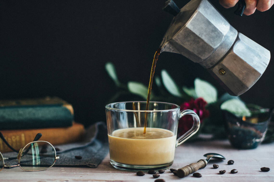 Kaffee wird aus einem Espressokocher in eine Glas-Tasse geschenkt