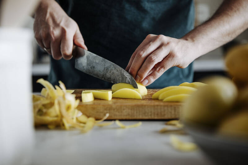 Kartoffeln geschnitten mit Hand und Messer vor dunklem Hintergrund.