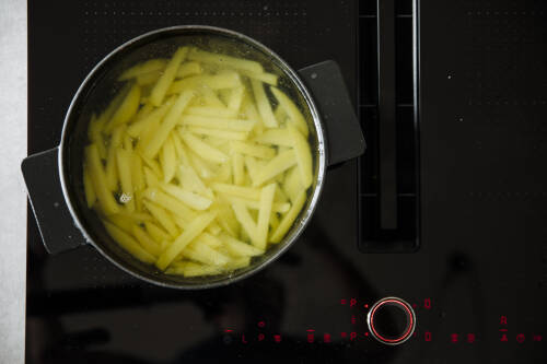 Kartoffeln in Scheiben geschnitten in Kochtopf auf Herd vor dunklem Hintergrund.