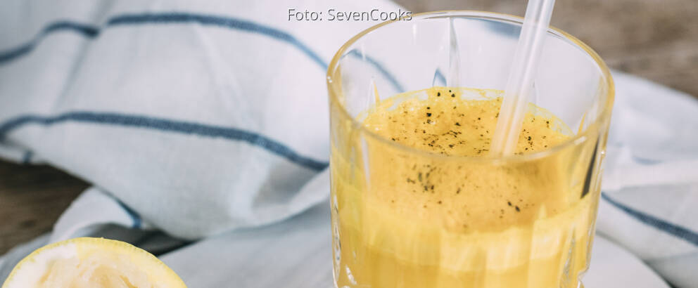 Gelber Kurkuma-Ingwer Immunbooster in Glas mit Strohhalm.