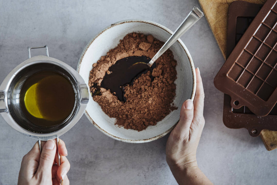 Margarine und Kakao in Schüssel und Topf mit Händen vor hellem Hintergrund.