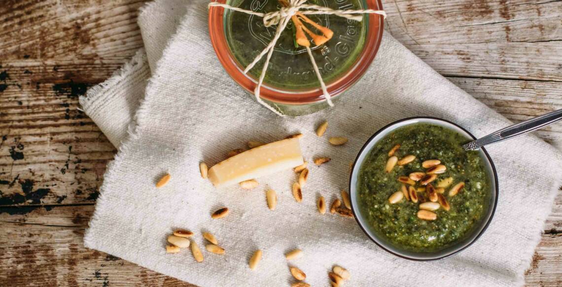 Pesto aus Pinienkernen, Parmesan und Karottengrün in einer Schale auf Holzhintergrund, von oben fotografiert.