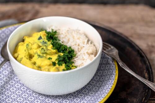 Curry mit Reis in einer Schüssel, darüber frische Kräuter. Daneben eine Gabel, von oben fotografiert.