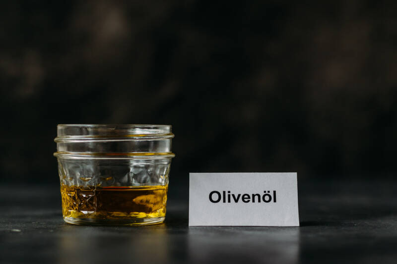 Olivenöl in Glas vor dunklem Hintergrund.