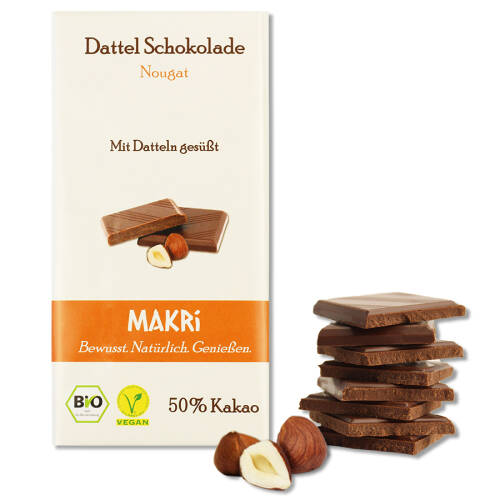 Eine Packung MAKRI-Schokolade Geschmacksrichtung "Nougat" - daneben Haselnüsse und Schokoladenstücke.