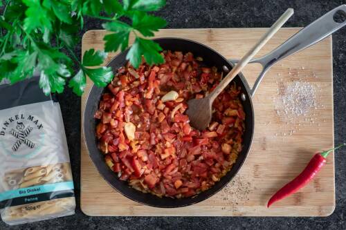 Tomatenwürfel in einer Pfanne mit Zwiebeln und Chilischoten.