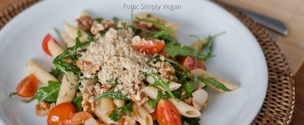 Teller mit Penne, Pucola, frischen Tomaten und veganem Parmesan