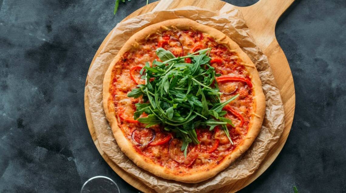Pizza mit veganem Käse, Tomaten und Rucola von oben fotografiert.