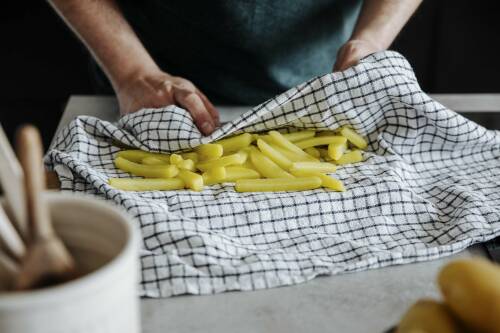 Pommes in Geschirrtuch mit Händen vor hellem Hintergrund.