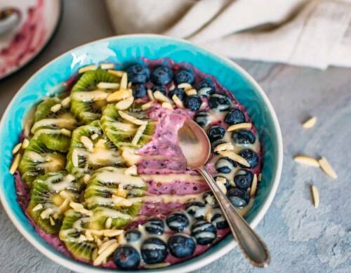 Quinoa-Frühstücksbowl mit Löffel in blauer Schüssel vor hellem Hintergrund.