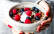 Schale in Händen mit Porridge, Himbeeren und Blaubeeren
