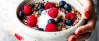 Schale in Händen mit Porridge, Himbeeren und Blaubeeren