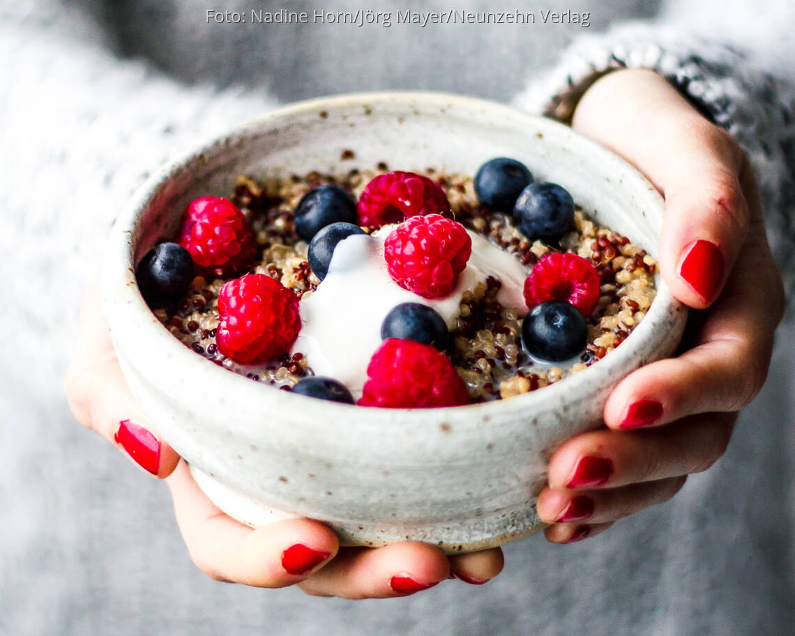 Schale in Händen mit Porridge, Himbeeren und Blaubeeren