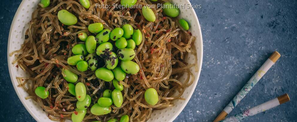 Weißer Teller mit rohen Kelp-Nudeln, Edamame und Esstäbchen