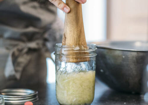 Selbstgemachtes Sauerkraut wird mit einem Holzstössel in ein Glas gedrückt.