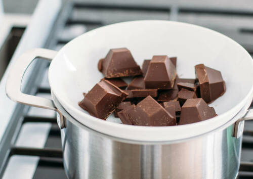 Schokoladestücke in einer weißen Schüssel, die in einem Topf steht.
