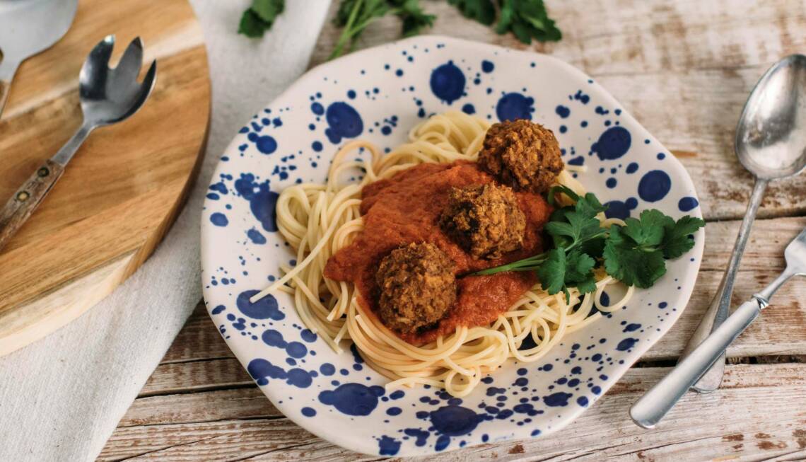 Blau-weißer Teller mit Spaghetti, Tomatensoße und Bällchen auf Seitanbasis gefüllt. Als Deko Petersilie, daneben Besteck. Von oben fotografiert.