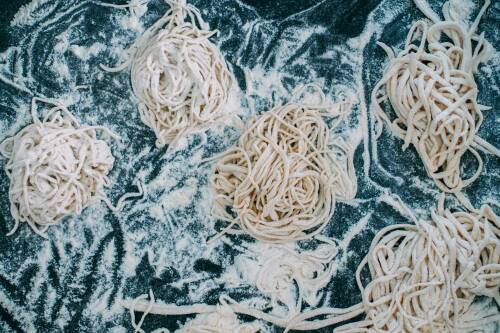 Mehrere kleine Spaghetti-Nester mit Mehl bestäubt, von oben fotografiert.